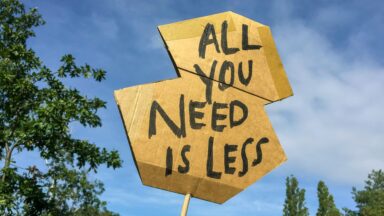 Skilt med træ i baggrunden, der viser "All you need is less"