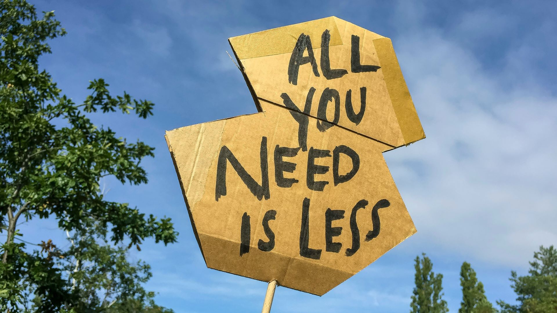Skilt med træ i baggrunden, der viser "All you need is less"